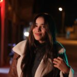 Night portrait of a woman with long hair smiling in an urban setting.